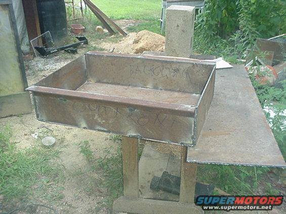 Metal box with "BACKHOE" and "FRONT" written on it, sitting on a workbench