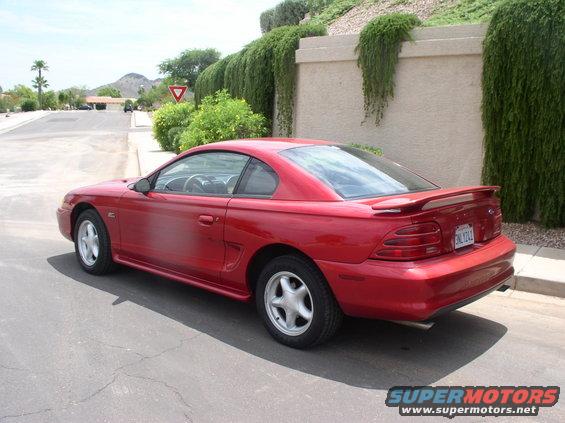 Red coupe parked on a residential street, showing its rear and side profile. The car has a spoiler and a license plate visible