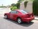 1995 Ford Mustang - A red coupe is parked on the side of a street with a landscaped wall and greenery in the background.