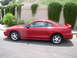 1995 Ford Mustang - A red coupe is parked outdoors with a wall and greenery in the background.