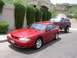 1995 Ford Mustang - A red 1995 Ford Mustang coupe is seen being towed by a lifted maroon SUV on a residential street.