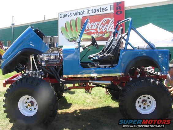 Blue off-road vehicle with large tires, exposed V8 engine, and roll cage, viewed from the side