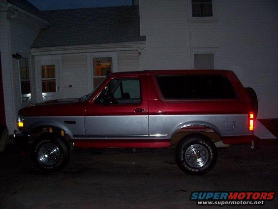Red and silver Ford Bronco, side view, parked at dusk