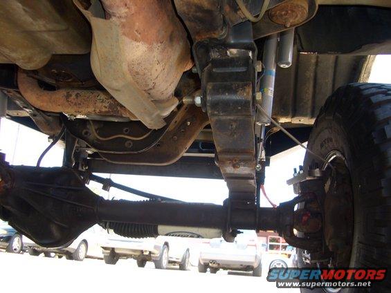 Undercarriage view showing leaf springs, differential, and exhaust system. Other vehicles visible in background