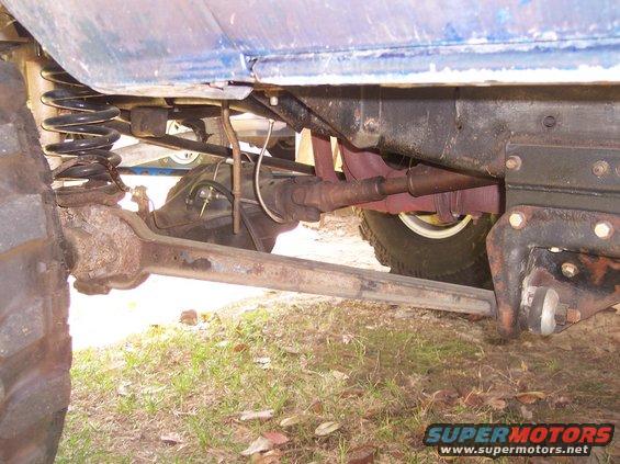 Undercarriage of a blue vehicle showing suspension, driveshaft, and rusty axle