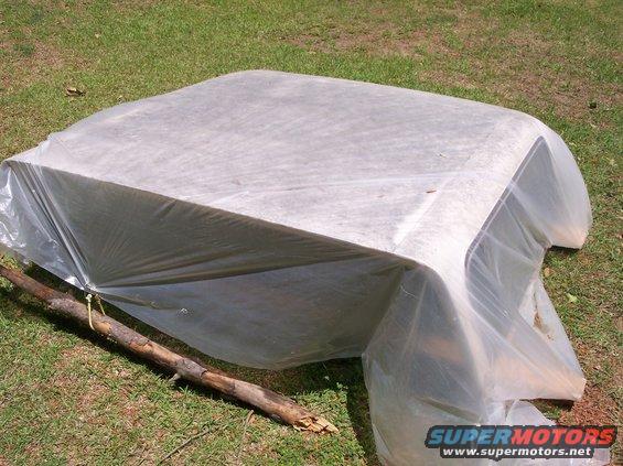 Car hardtop covered with white plastic sheeting and a branch propping it up