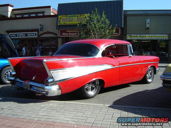 Red 1957 Chevrolet Bel Air parked on a brick sidewalk in front of shops