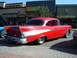 1990 Ford Thunderbird - A classic red Chevrolet Bel Air is parked on a street with shops in the background.