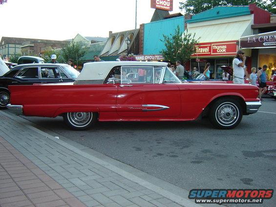 Red convertible with a white top parked on a street, side view