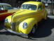 1990 Ford Thunderbird - A bright yellow coupe from the 1940s is parked on a street, with another vintage car visible to its left.