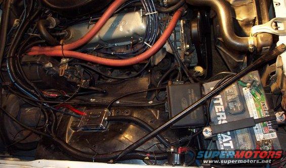 Engine bay showing battery, wiring, and engine components. Ford logo visible on a black box