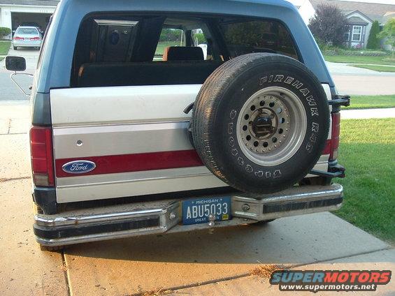 Rear view of a blue and silver Ford Bronco with a spare tire mounted on the back. The vehicle has a red stripe and a Michigan license plate