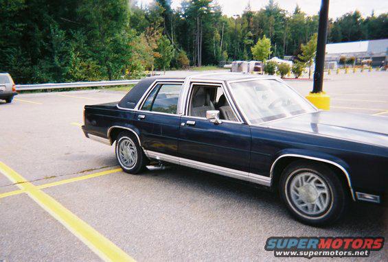 Dark blue sedan parked in a lot, showing its side and front quarter panel. Chrome trim accents the body