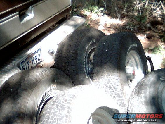 Spare tires piled up next to a vehicle's rear bumper and license plate reading 6TP H92