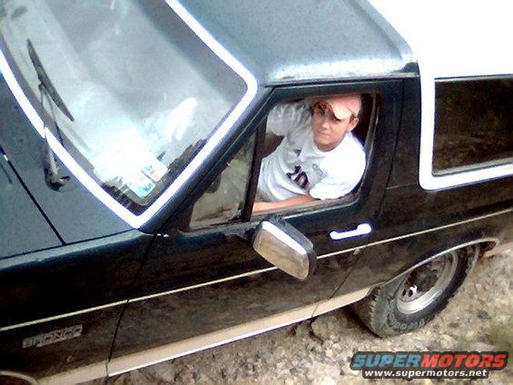 Side view of a dark green Ford Bronco, possibly from the early 80s, with a person leaning out the window