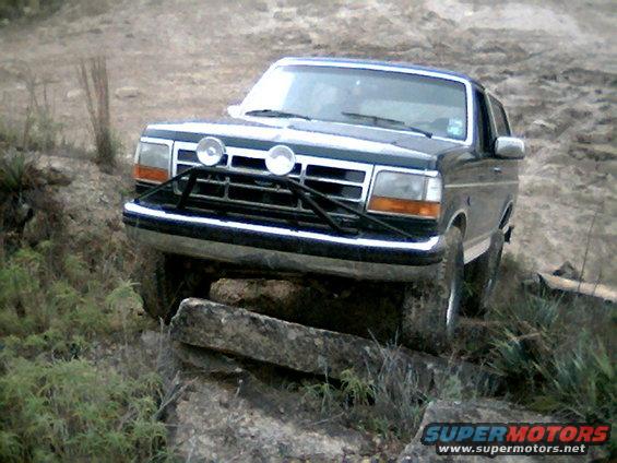 1992 Ford Bronco front view, navigating rocky terrain with a brush guard and auxiliary lights