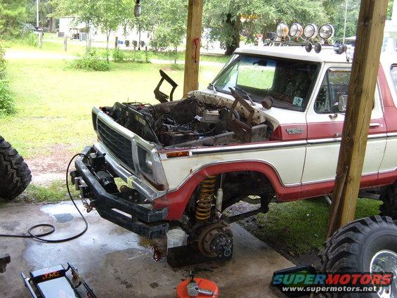White and red Ford Bronco with hood open, undergoing repairs