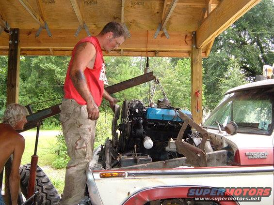 Two guys working on removing an engine from a Bronco SUV with an engine hoist