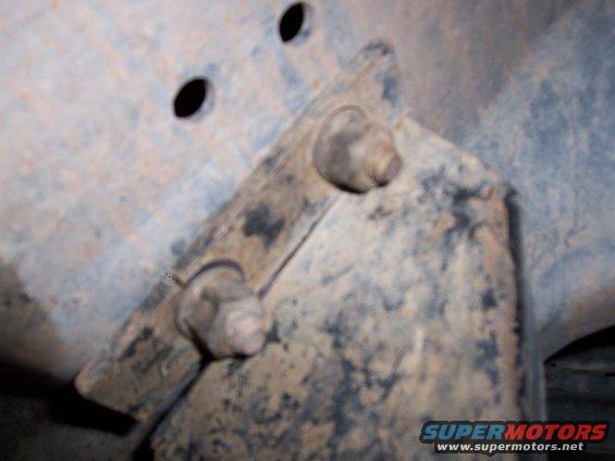 Rusty metal frame bracket with two bolts, part of a vehicle's undercarriage