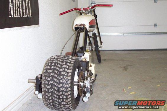 Custom motorized bike with huge rear tire, red handlebars, and white gas tank. It's in a garage