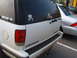 1988 Ford Bronco - A white Chevrolet SUV is parked next to a silver sedan, displaying several decals on its rear window.