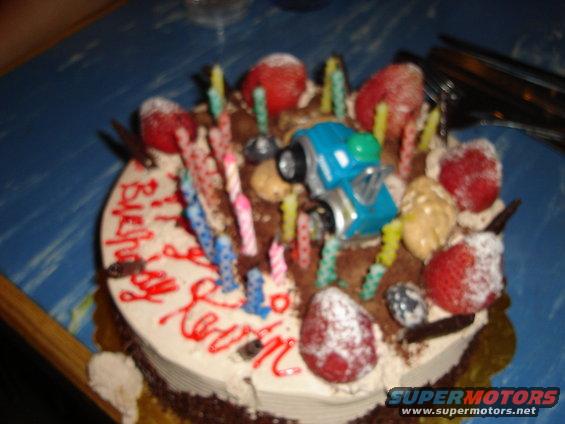 Blue toy truck on a birthday cake with strawberries and candles
