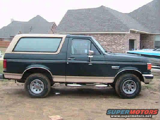 1988 Ford Bronco parked on dirt, side view. Tan removable top