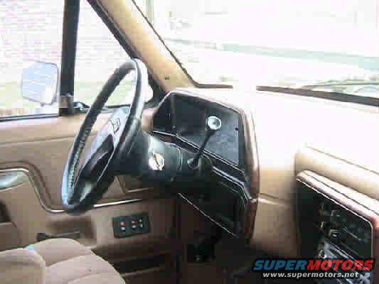 Interior shot of a vehicle's dashboard, steering wheel, and door panel. Shows a tan interior with black accents
