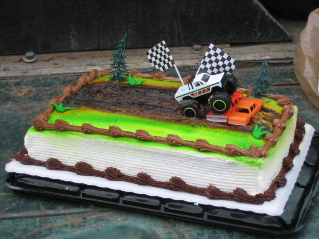 Toy monster truck and orange car on a cake decorated like a race track