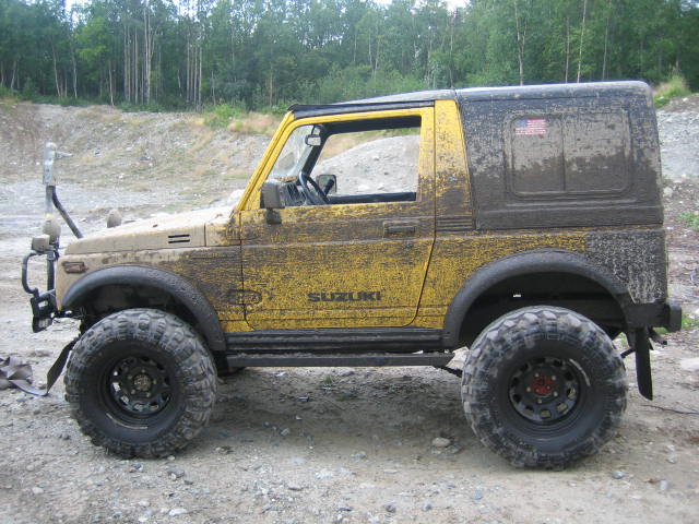 Mud-covered 1987 Suzuki Samurai, side view. Yellow paint with black hardtop. Large off-road tires