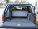 1995 Ford C-350 (Centurion Conversions) - Rear view of a blue van's interior, showing folded seats, a spare tire, and carpeting. A Supermotors.net logo is present.