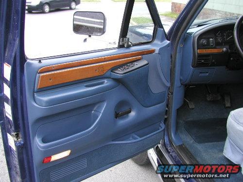 blue interior door panel with wood trim and power window controls, dashboard visible, other car outside