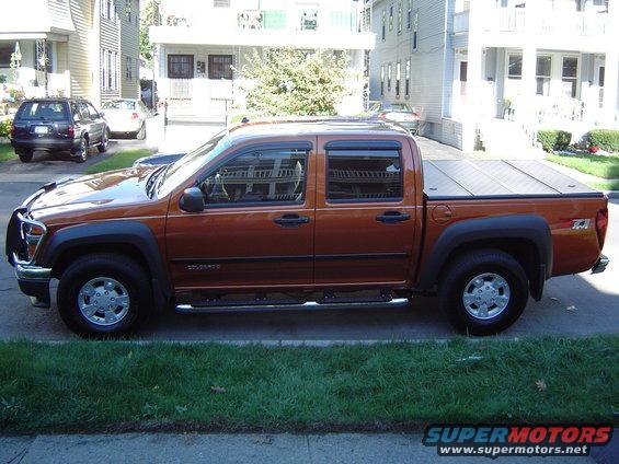 2004 Chevrolet Colorado pickup truck, side view. Orange paint, four doors, tonneau cover