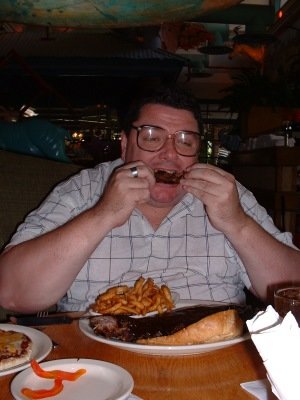 Man with glasses eating ribs and fries at a table
