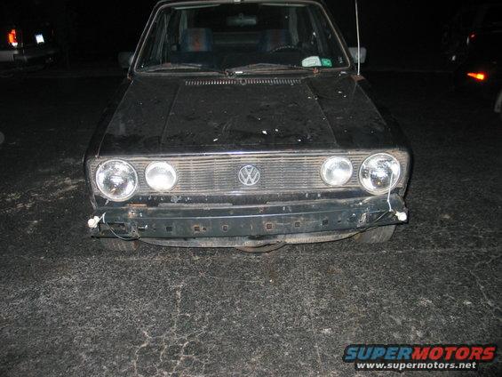 Black Volkswagen Golf Mk1 front end, missing front bumper section. Another car is visible to the left
