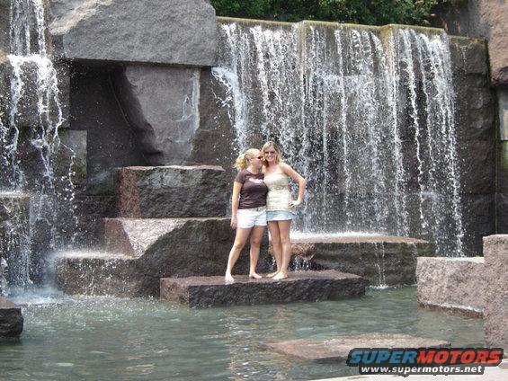 Two women stand on rocks near a cascading waterfall