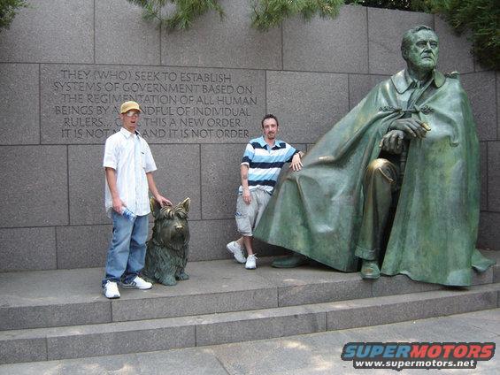 Two people and a dog sculpture pose with the Franklin D. Roosevelt Memorial statue