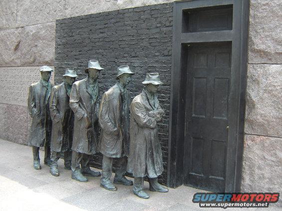 Bronze statues of men in line before a dark door, with stone and brick wall background