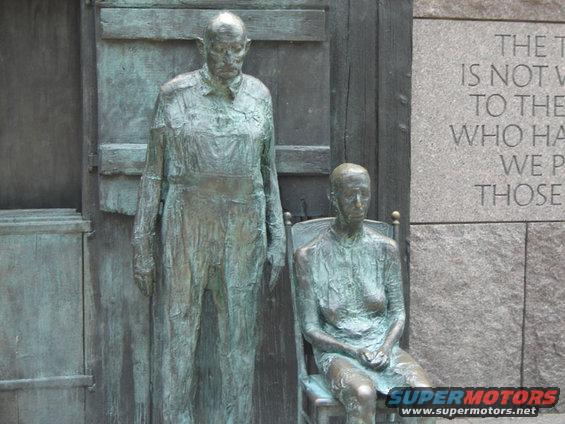 Bronze statues of a man and woman with engraved text on a stone wall