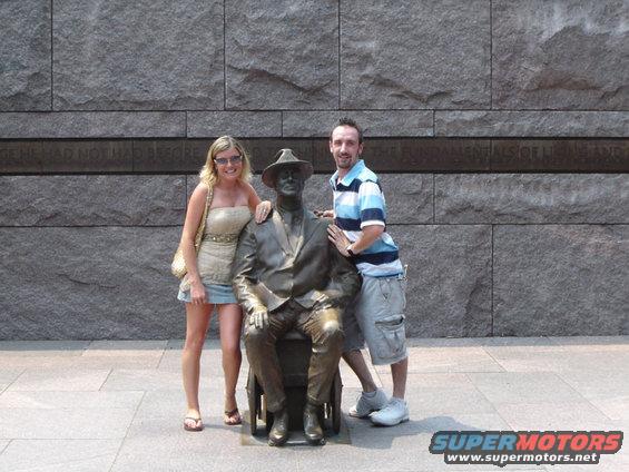 Couple posing with FDR statue in wheelchair. Stone wall behind them