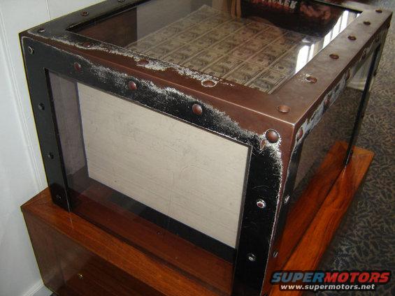 Coffee table with glass top displaying US currency, riveted metal frame, and wooden base
