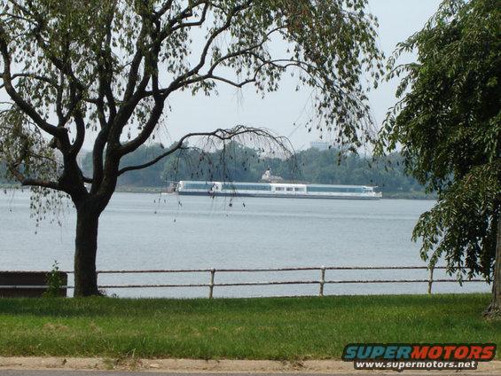 Long white boat on a body of water, seen through trees and grass