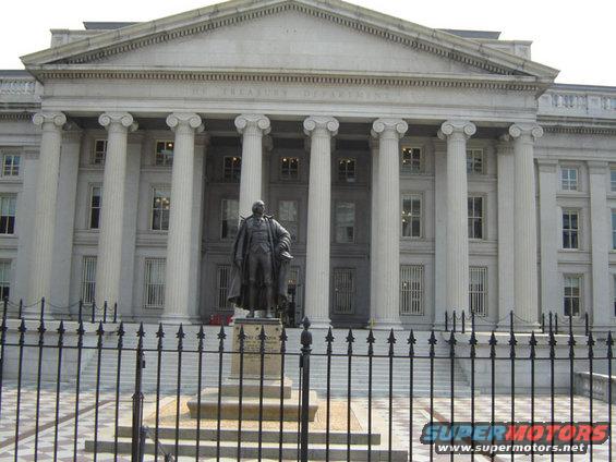 Treasury Department building with columns and a statue in front, behind a black fence