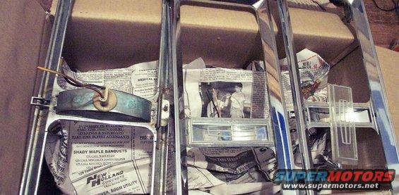 Chrome trim pieces, possibly for a car, wrapped in newspaper inside a cardboard box