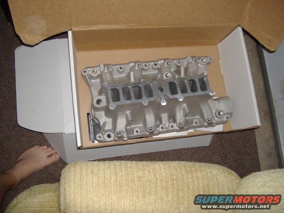 New Edelbrock intake manifold in a box, sitting on carpet next to a couch. A foot is visible on the left