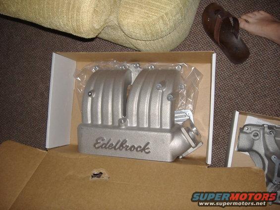 Silver Edelbrock intake manifold in a cardboard box, partially wrapped in plastic