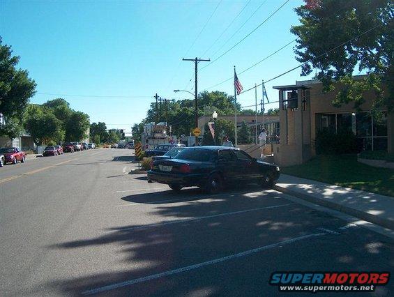 Dark sedan parked on street next to a building with an American flag