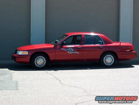 Red sedan, looks like a police car, parked outside a building