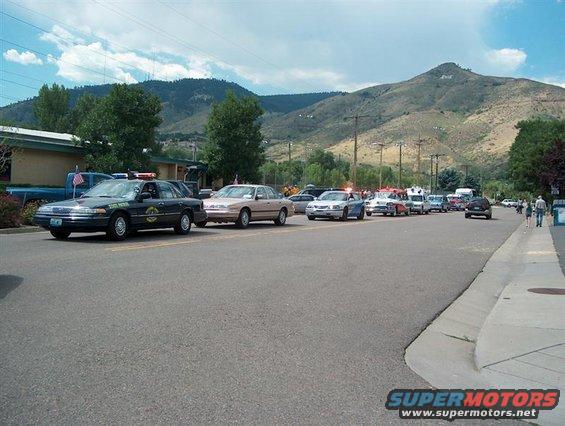 Police car and other vehicles lined up on a street with mountains in the background