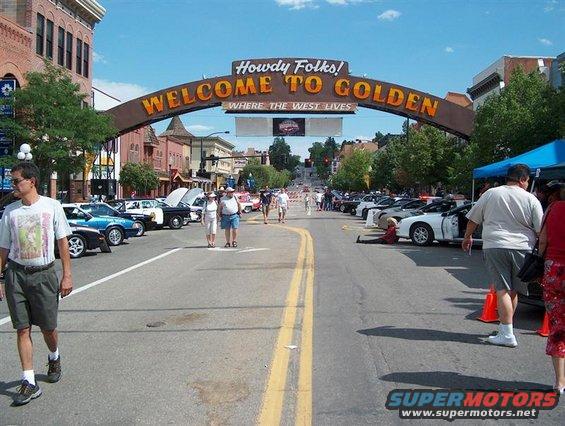 Welcome to Golden sign over a street lined with parked cars and people